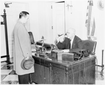 Photograph of White House receptionist William Simmons at his desk, conversing with an unidentified visitor. - NARA - 199477 photo