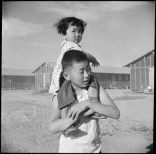 Poston, Arizona. A little evacuee of Japanese descent gets a ride on her brother's shoulders at thi . . . - NARA - 538565