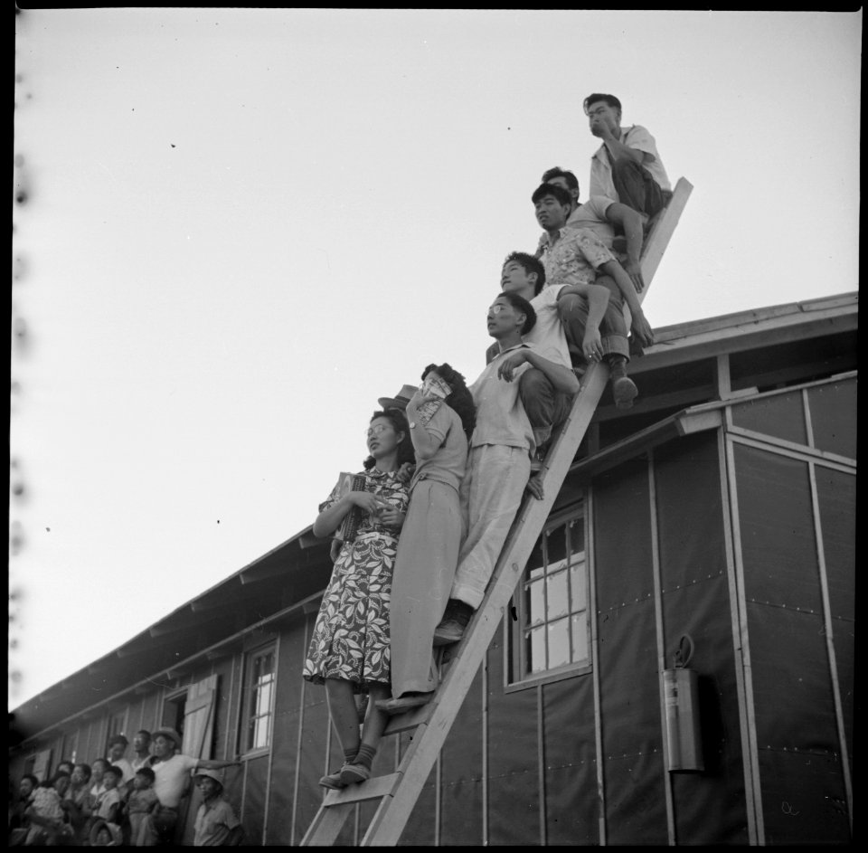 Poston, Arizona. Evacuees of Japanese ancestry on odd perch watching an outdoor musical show at thi . . . - NARA - 538563