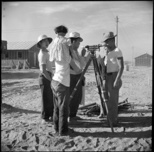 Poston, Arizona. Evacuees of Japanese ancestry watch fellow evacuee surveyors at work at this War R . . . - NARA - 538566 photo