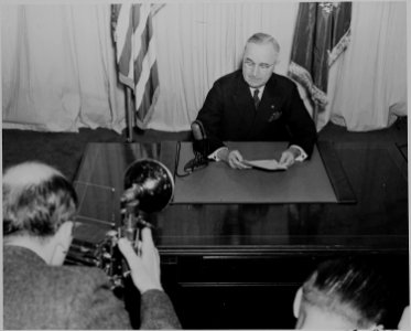 President Harry S. Truman seated at a desk, before a microphone, announcing the end of World War II in Europe. A... - NARA - 199076