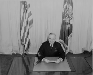 President Harry S. Truman seated at a desk, before a microphone, announcing the end of World War II in Europe. - NARA - 199075