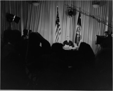 President Harry S. Truman seated at a desk, lights on, cameras rolling, announcing that World War II in Europe has... - NARA - 199079