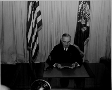 President Harry S. Truman seated at a desk, before a microphone, announcing the end of World War II in Europe. - NARA - 199078