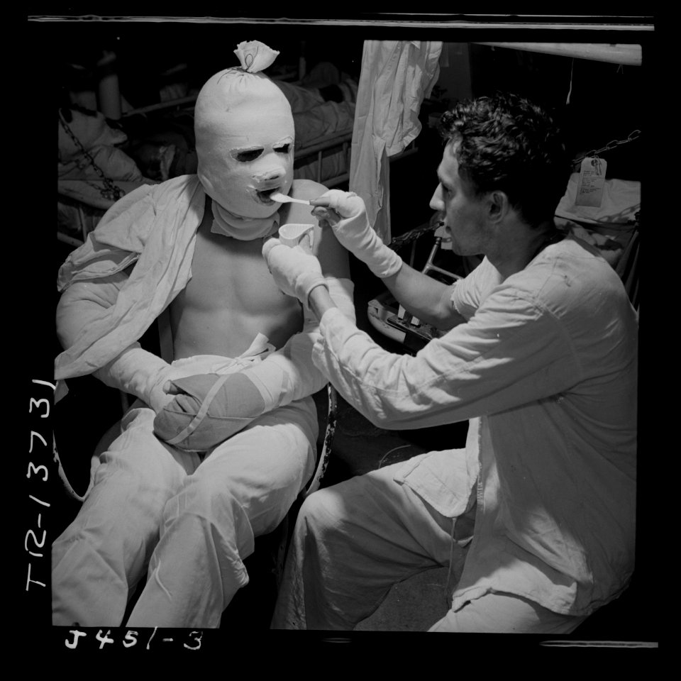 Pressure bandaged after they suffered burns when their ship was hit by a kamikaze attack, men are fed aboard the USS... - NARA - 520693