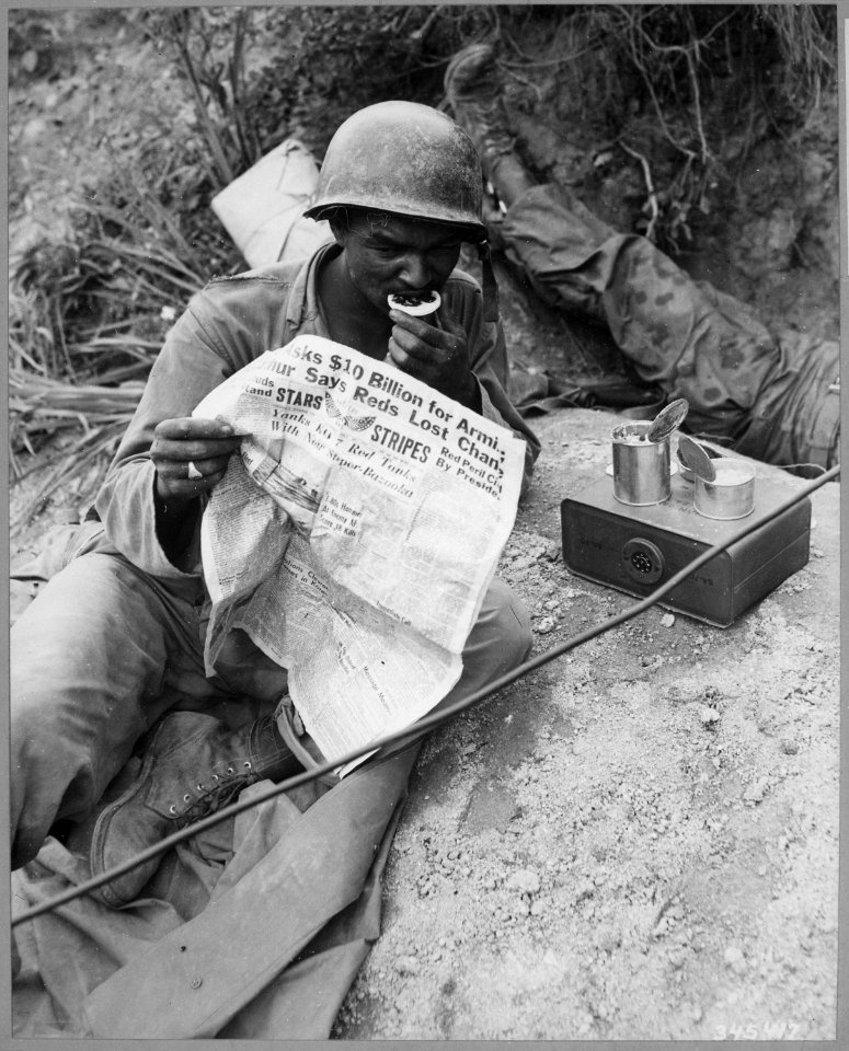 Private First Class Clarence Whitmore, voice radio operator, 24th Infantry Regiment, reads the latest news while... - NARA - 541945