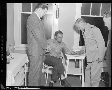 Rear Admiral Joel T. Boone examines arm of John Ketchum, drilling contractor, as Dr. W. S. Gibson, company doctor... - NARA - 540320