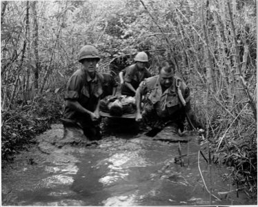 Soldiers carry a wounded comrade through a swampy area. - NARA - 531457 photo