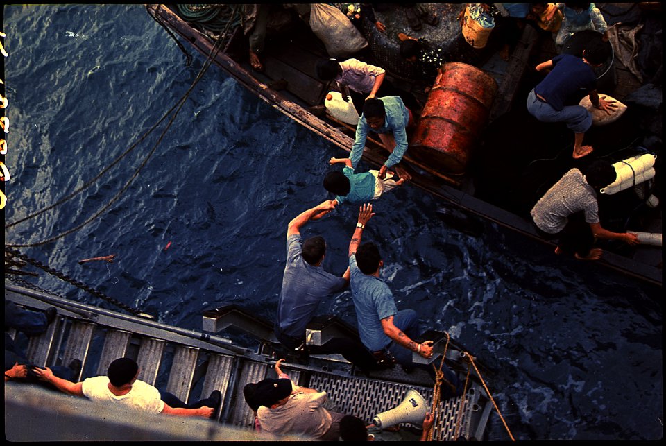 South China Sea....Crewmen of the amphibious cargo ship USS Durham (LKA-114) take Vietnamese refugees aboard a small... - NARA - 558518