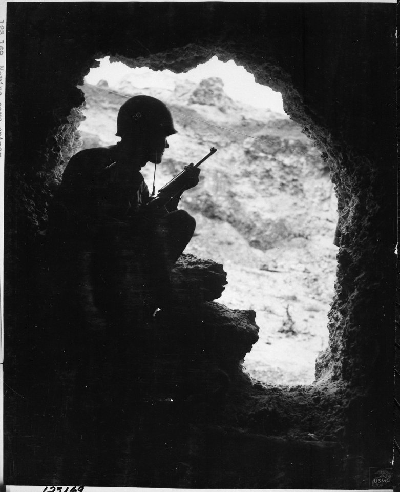 Silhouetted against the entrance to one of the caves that honeycomb the Okinawa hills, a Marine rifleman resorts to... - NARA - 532558