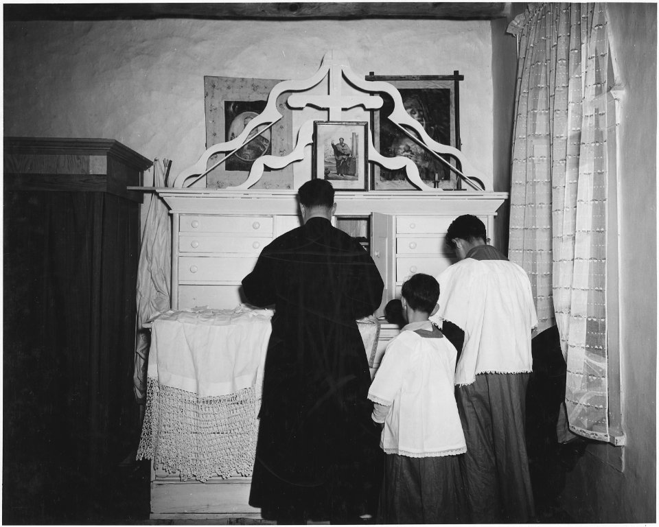 Taos County, New Mexico. Father Morgan puts on vestments for Mass in vestry of church at Arroyo Hon . . . - NARA - 521913