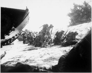 The first wave of Marines to hit the Saipan beach in the Marianas invasion take cover behind a sand dune, while... - NARA - 532527