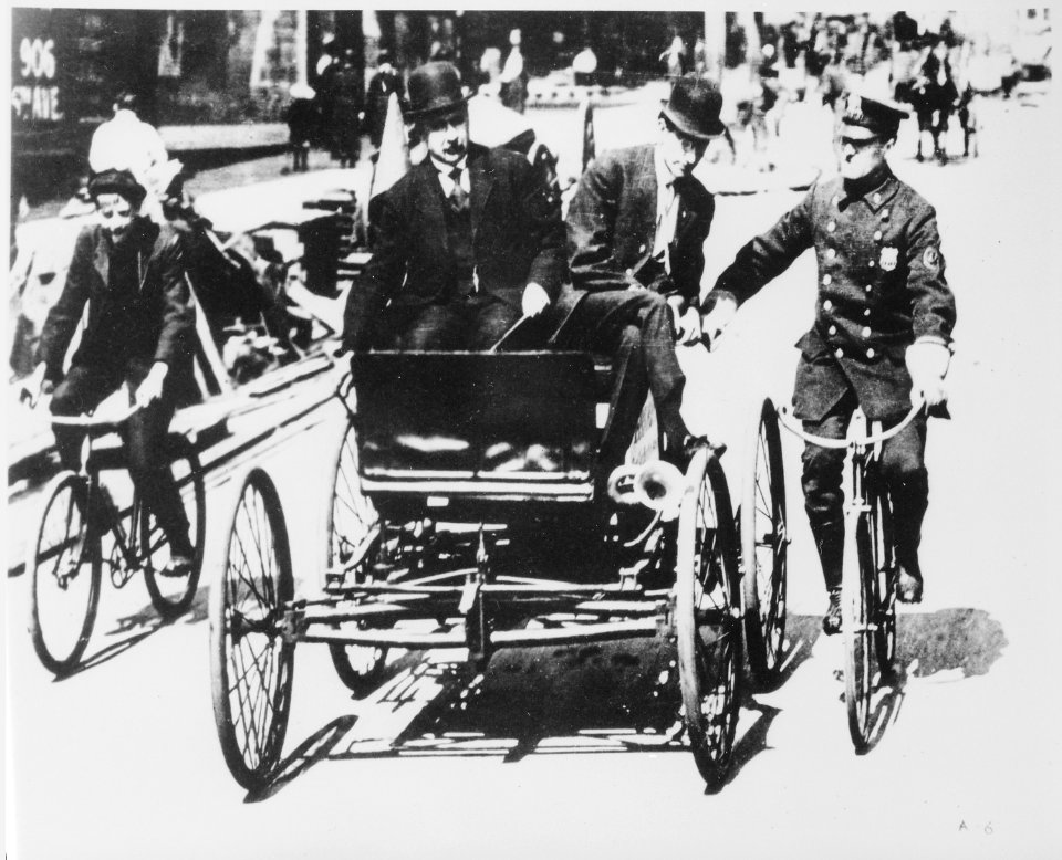 Traffic violator driving a 1900-vintage car being stopped by a policeman on a bicycle, 1949 - NARA - 513352