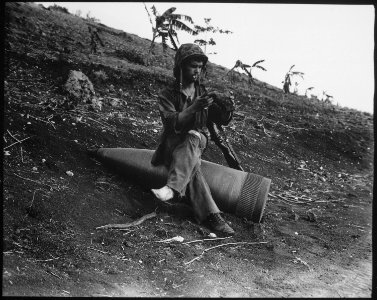Using an unexploded 16-inch naval shell for a resting place, Marine Private First Class Raymond Hubert, shakes a... - NARA - 532530