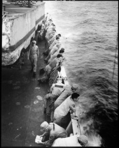 U.S. Marines stand along the rail and watch the ocean aboard the USS Clymer. To the aft a Marine is washing his... - NARA - 532397