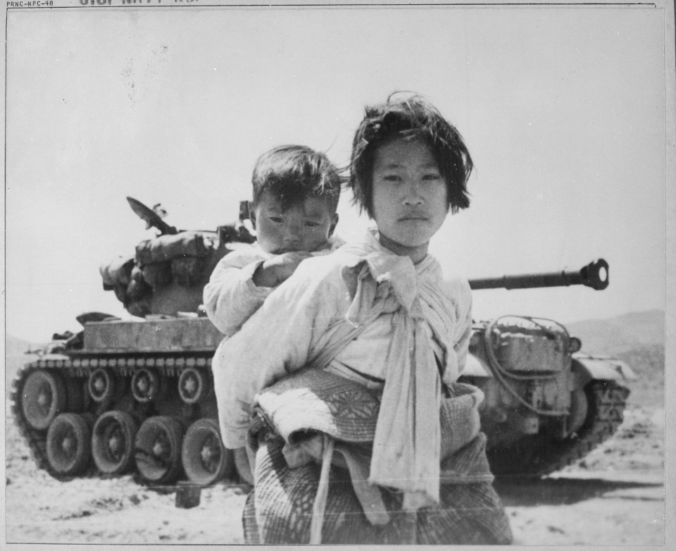 With her brother on her back a war weary Korean girl tiredly trudges by a stalled M-26 tank, at Haengju, Korea. - NARA - 520796