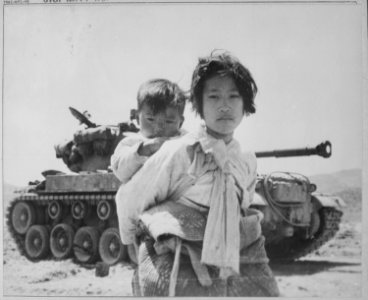 With her brother on her back a war weary Korean girl tiredly trudges by a stalled M-26 tank, at Haengju, Korea. - NARA - 520796 photo