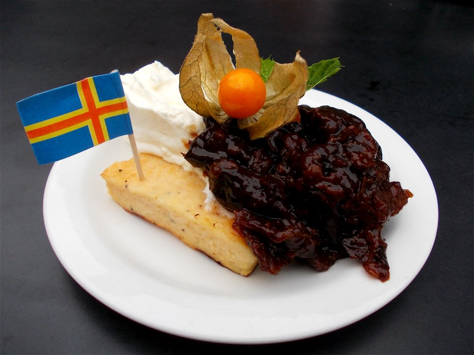 Ahvenanmaan pannukakku (Ålandspannkaka) served with whipped cream and plum jam, topped with a Physalis peruviana and the flag of the autonomous region of Ahvenanmaa.