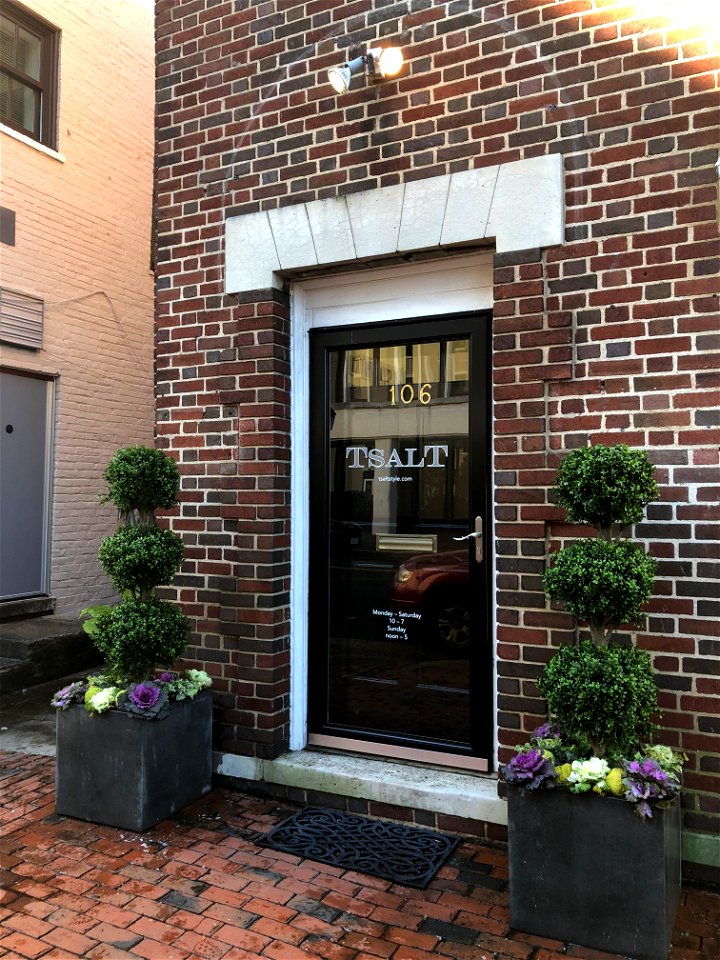 Flower pots with three-ball topiaries; white, wine and green ornamental cabbages and Osage oranges adorn entrance to boutique shop.