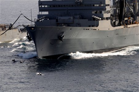 Dolphins playfully jump out of the water off the bow of the Military Sealift Command fast combat support ship USNS Bridge during a replenishment at sea between Bridge and the Ticonderoga-class guided-