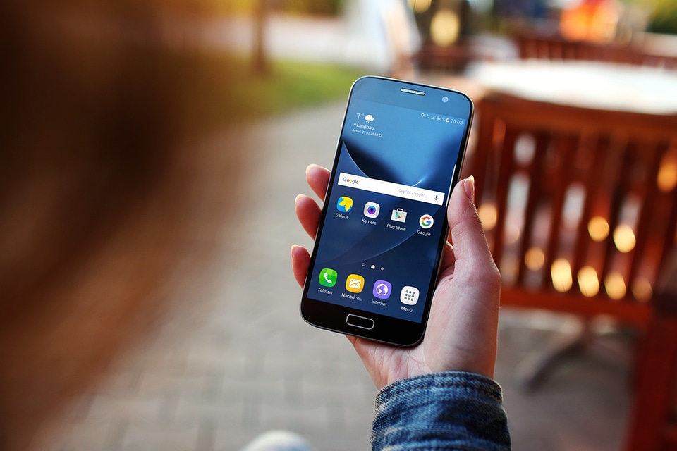 A young woman uses her smartphone Galaxy S7 outside on the pavement café
