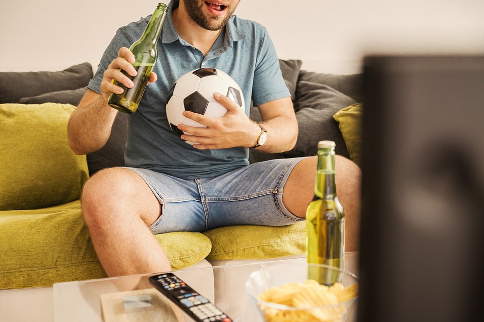 1 Young man watching football on TV and drinking beer at home