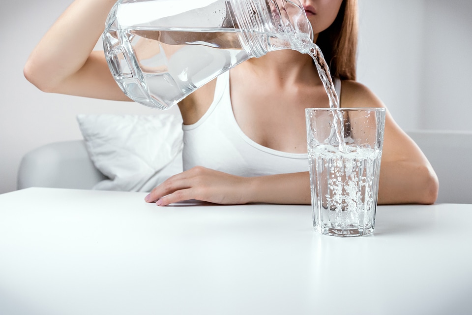 Close up of young girl pouring fresh pure water from pitcher into a glass