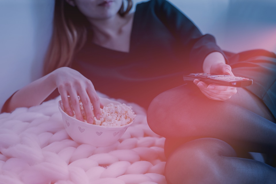 Woman is watching TV and eats a popcorn from bowl photo
