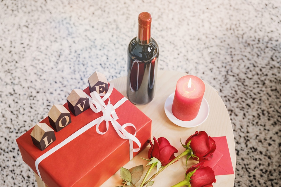 Wooden table with bottle of wine, roses and gift box photo