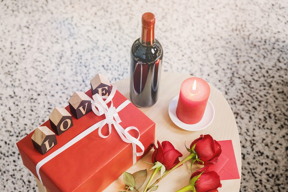 Wooden table with bottle of wine, roses and gift box