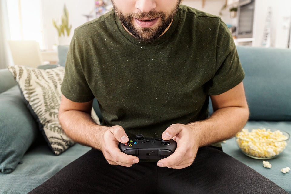 Close up of man eats popcorn, holding joy stick and playing video games on tv at vacation, sits at home on the couch.