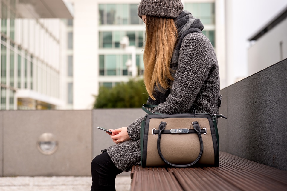 woman sitting on bench outside and using smartphone