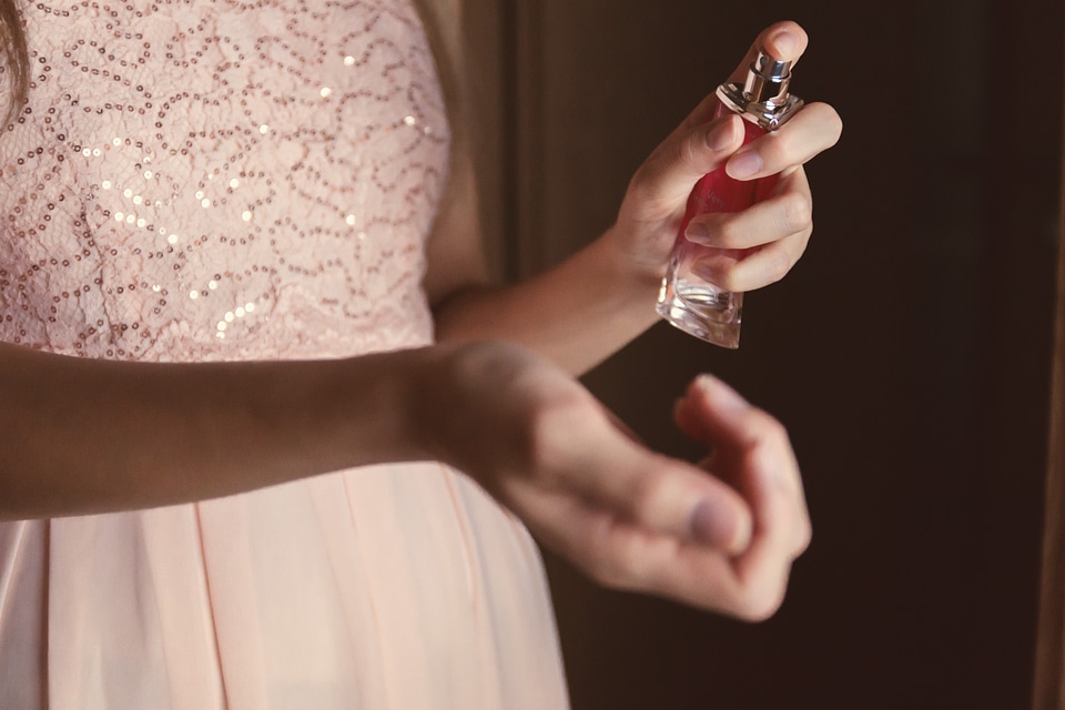Beautiful young woman with bottle of perfume at home, closeup