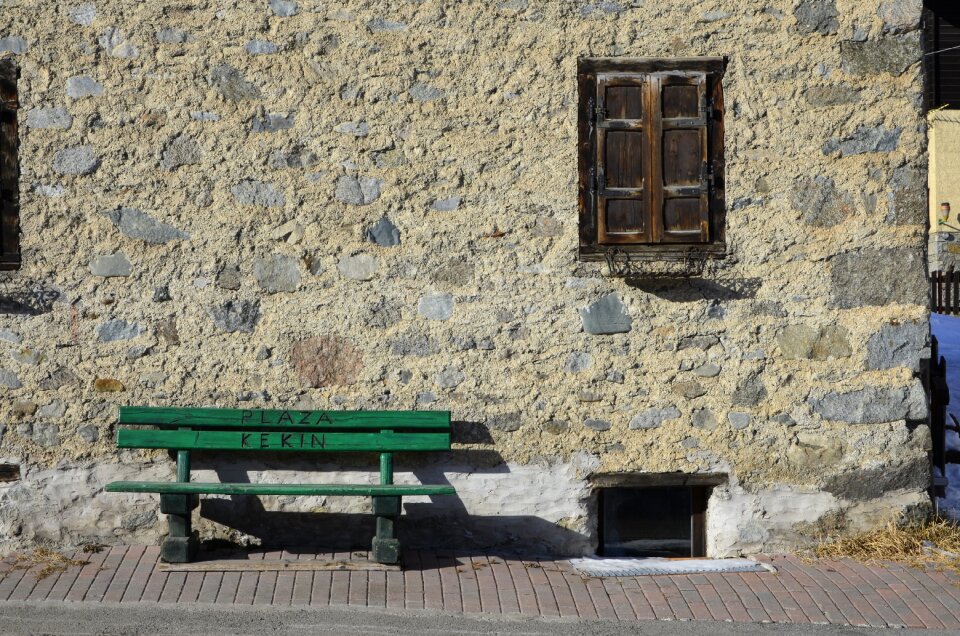 Green bench in front of the house wall of stone