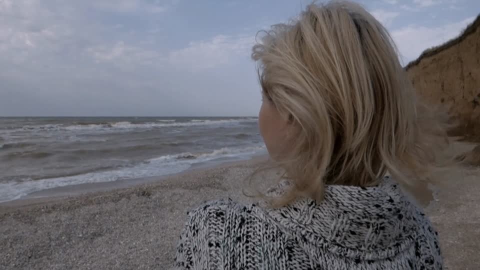 A woman stands on the seashore thoughtfully looks sad into the distance