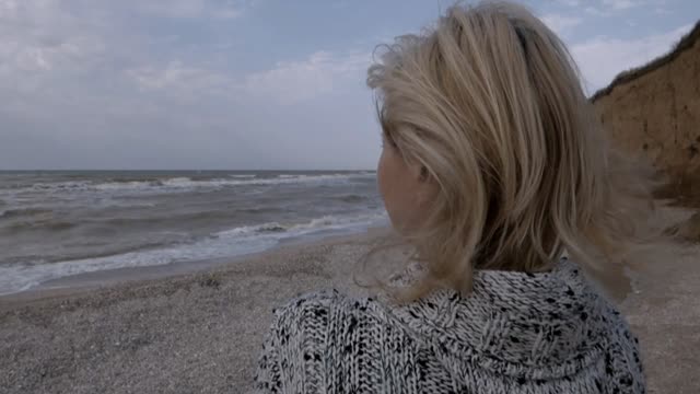 A woman stands on the seashore thoughtfully looks sad into the distance