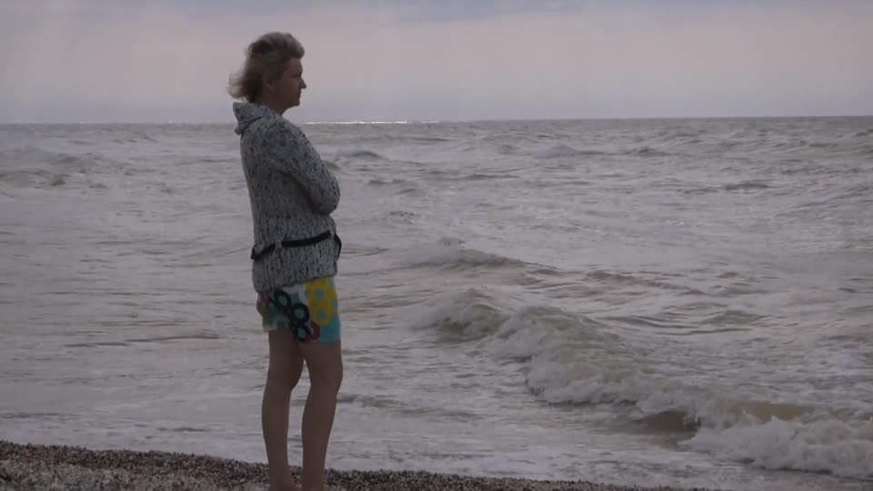 A woman stands on the seashore thoughtfully looks sad into the distance